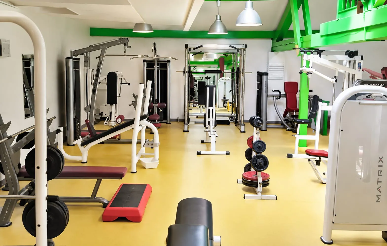 Plateau lumineux de musculation avec machines guidées, bancs et poids.